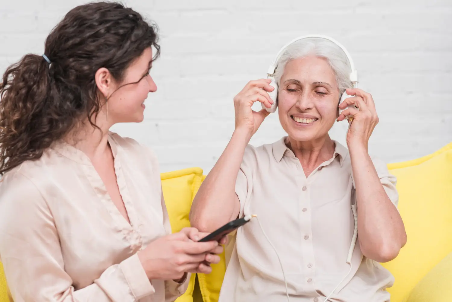Filha segurando o celular enquanto a mãe ouve música com fones de ouvido.